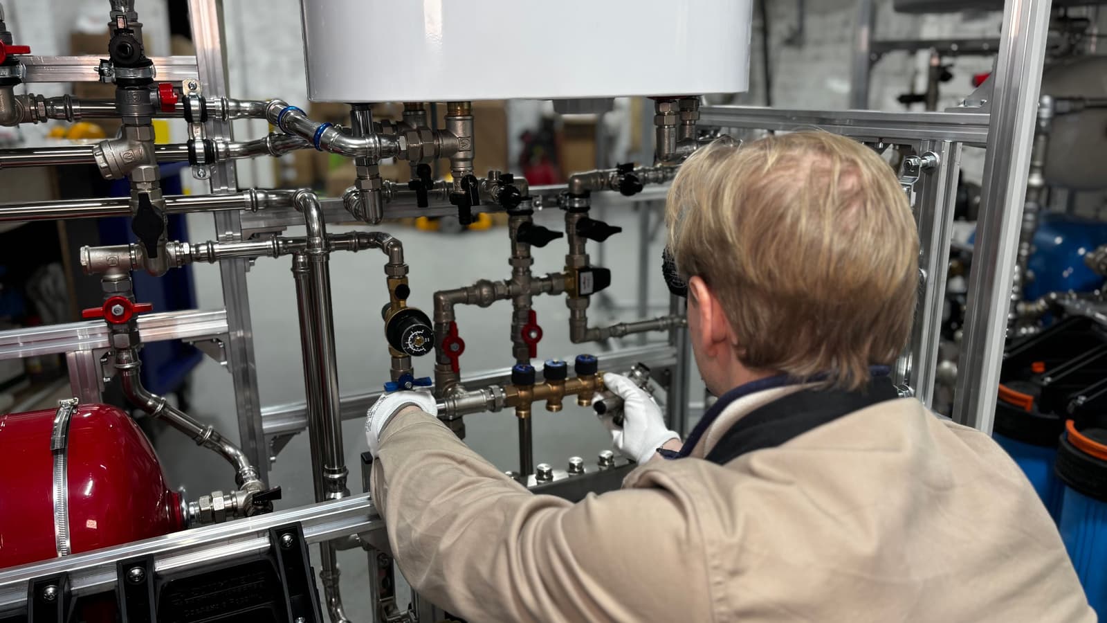 Technician in gloves working on a manifold of pipes, valves and fittings in a mechanical room